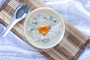 Rice porridge or congee with egg in white bowl and spoon on wooden table