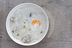 Rice porridge or congee with egg in white bowl on vintage wooden table.