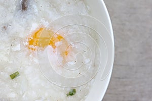 Rice porridge or congee with egg in white bowl on wooden table background.