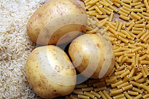 Rice, potatoes and macaroni pasta on a wooden table.Three common carbohydrates which provide energy but can cause obesity