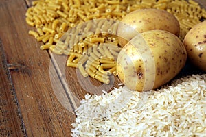 Rice, potatoes and macaroni pasta on a wooden table. Three common carbohydrates which provide energy but can cause obesity