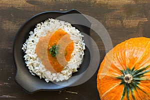 Rice with pumpkin sauce on black plate on wooden background