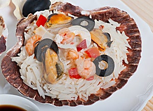 Rice in the shell, decorated with seafood, shrimps, mussels, squid rings and olives.