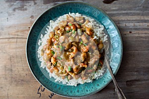 Rice smothered with homemade crawfish etouffee. Shown with whole boiled crawfish and green onions on a wood background.