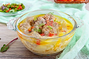 Rice soup with meat balls and vegetables in a transparent glass bowl.