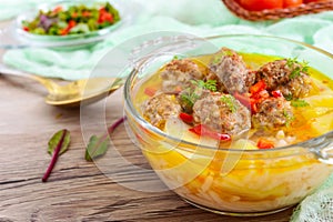 Rice soup with meat balls and vegetables in a transparent glass bowl.