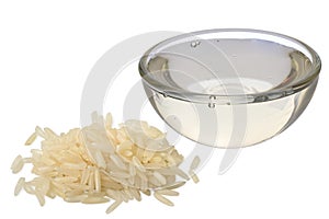 Rice syrup in a glass bowl next to a pile of uncooked white rice isolated on white