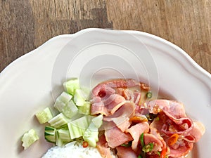 Rice topped with stir-fried pork and basil and cucumber In a white plate on a wooden table