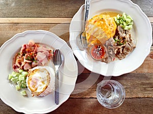 Rice topped with stir-fried pork and basil and cucumber In a white plate on a wooden table