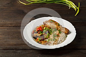 Rice with vegetables in sauce and chicken leg in a white plate on a wooden table