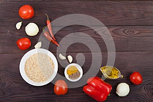Rice, vegetables and spices for cooking jollof rice on brown wooden background. Copy spaes