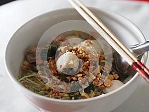 Rice Vermicelli soup with pork balls in white bowl on top prinkle roasted peanuts chopstick spoon