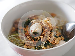 Rice Vermicelli soup with pork balls in white bowl on top prinkle roasted peanuts spoon