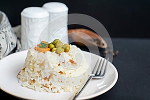 Rice in white plate and carrot and pea grains on it with black wooden background