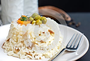 Rice in white plate and carrot and pea grains on it with black wooden background