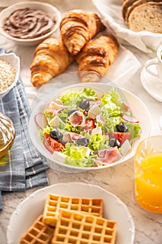 Rich breakfast assortment with salad, croissants, waffles, bread and orange juice