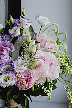 Rich bunch of pink peonies peony and lilac eustoma roses flowers in glass vase on white background. Rustic style, still