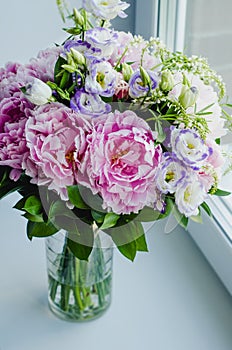 Rich bunch of pink peonies peony and lilac eustoma roses flowers in glass vase on white background. Rustic style, still