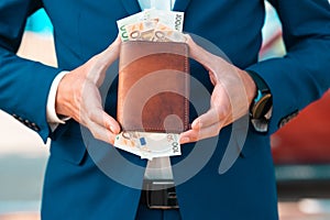 Rich businessman in a blue jacket shows off a leather brown wallet full of euro cash. Close-up of the hands. The concept