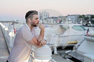 Rich businessman dreaming and thinking near the yacht. Portrait of stylish male model outdoor. Fashion male posing near