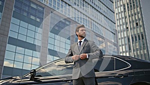 Rich businessman posing car buttoning jacket. Elegant man standing urban street