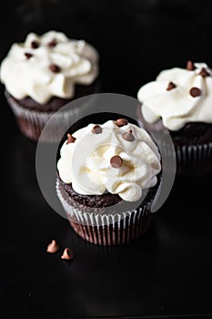 Rich chocolate cupcakes with whipped cream frosting and chocolate chips on a balck background