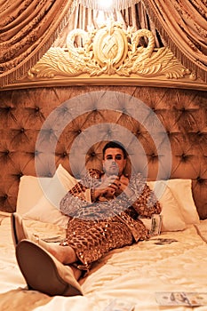 Rich and eccentric man dressed in a shimmering golden suit with a lot of US dollar bills in a royal, luxurious suite