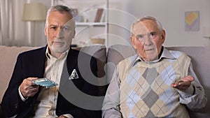 Rich elderly man showing bunch of dollars, poor senior friend showing coins