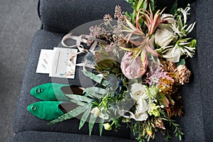 Rich green wedding bouquet with pink ribbons on the grey armchair. Green bridal shoes, and a wedding complimentary lying near the