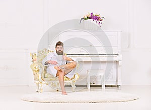 Rich guy sitting in armchair and drinking tea or coffee. Bearded guy in white room. Perfect morning concept