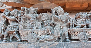 Rich indian people traveling by horse carts, on wall with old relief. 12th century Hindu Hoysaleshwara temple in India