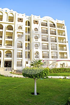 Rich luxury modern residential apartment hotel facade, tropical resort with green grass lawn on warm sunny day outdoor