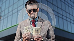 Rich man in Stylish Suit Wearing Sunglasses Counting Money and Walking in the Street near Office Building