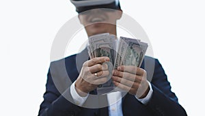 Rich man wearing VR headset counting money and smiling. Young businessman standing with pack of dollars. Richness and