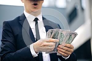 Rich man wearing VR headset counting money and smiling. Young businessman standing with pack of dollars. Richness and