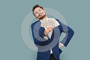 Rich proud satisfied man with mustache standing showing fan of dollars banknotes, keeps hand on hip.