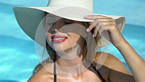 Rich woman in big white hat standing in pool, luxury resort hotel, wellness