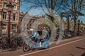 Rickshaw riding on street beside canal and old buildings in sunny day at Amsterdam.