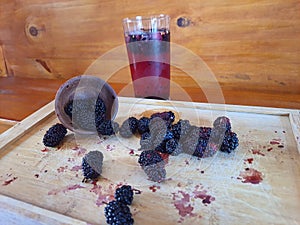 Blackberry caipirinha in a transparent glass cup, with some ripe blackberries on a wooden board on a wooden background. photo
