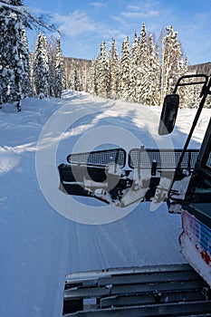 A ride in the cabin of an open red snowcat, a view of the caterpillar of a snowcat on a snowy road in the forest.