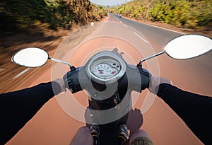 Rider driving scooter on an asphalt road. Motion blurred background. First-person view.