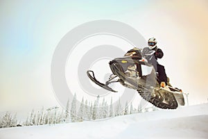 The rider in gear with a helmet making flying jumping taking off on a snowmobile on a background of a winter scenic landscape with