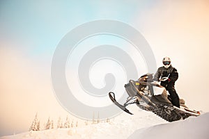 The rider in gear with a helmet making snow jumping on a snowmobile on a background of a winter scenic landscape with mounting and