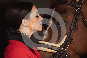 Rider jockey woman hugs with brown horse, black background