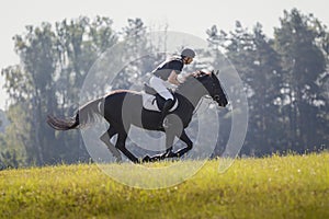Rider man and black stallion horse galloping during eventing cross country competition