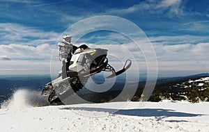 RIDER MAN WITH HELMET JUMPING WITH A SNOWMOBILE IN THE SUMMIT IN WINTER