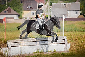 Rider man jumping drop fence obstacle on black stallion horse during eventing cross country competition