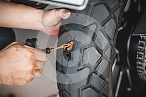 Rider use a tire plug kit and trying to fix a hole in tire`s sidewall ,Repair a motorcycle flat tire in the garage. motorcycle photo