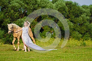 Rider woman blonde with long hair in a white dress with a train posing on a palamino horse
