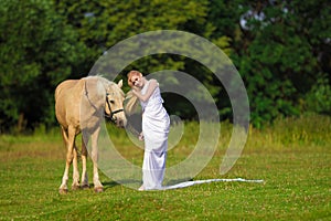 Rider woman blonde with long hair in a white dress with a train posing on a palamino horse